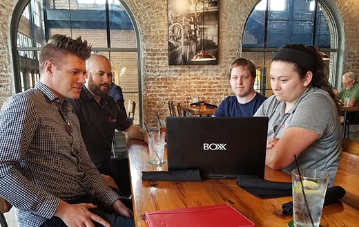 a group of people at a restaurant all looking at the screen of a BOXX laptop